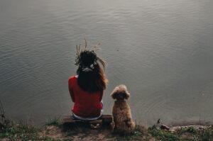 Woman and dog sitting calmly together by a lake, reflecting learning self-trust as an animal carer